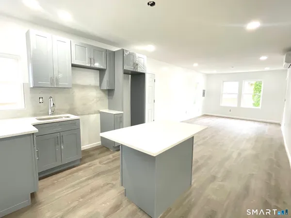 a large kitchen with stainless steel appliances a large kitchen island a sink dishwasher a stove and white cabinets with wooden floor