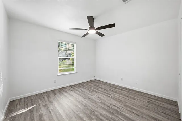 an empty room with wooden floor ceiling fan and window