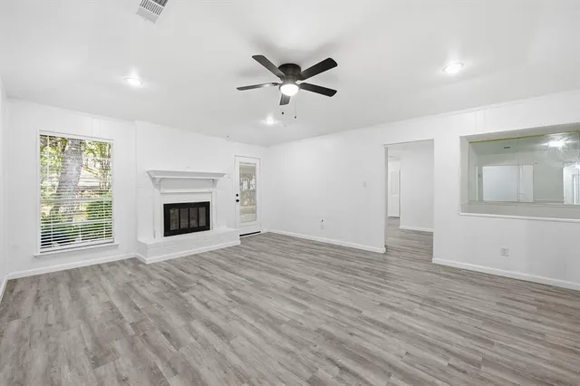 a view of an empty room with wooden floor fireplace and a window