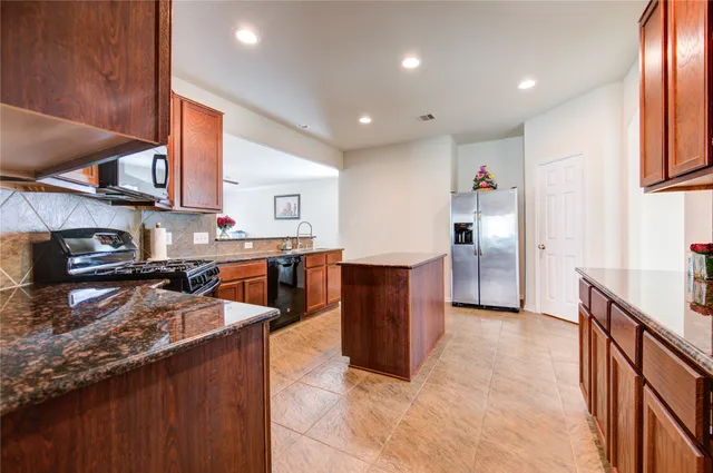 a kitchen with stainless steel appliances granite countertop a stove top oven a sink dishwasher and a refrigerator with wooden cabinets