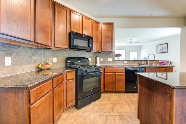 a kitchen with stainless steel appliances granite countertop a stove a sink dishwasher a microwave oven and a refrigerator with wooden cabinets