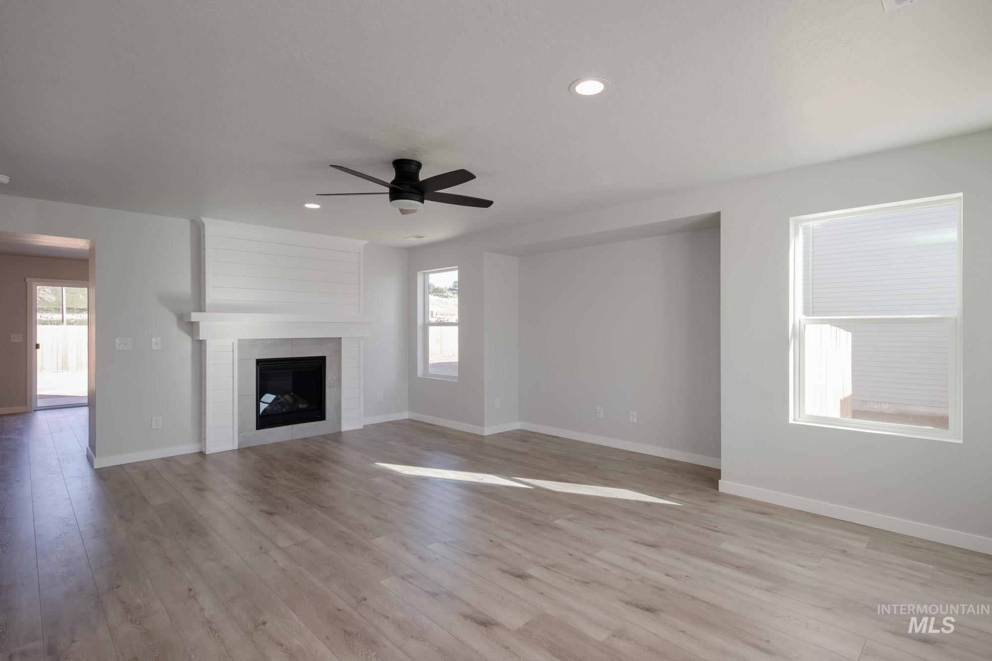 1732 Webb Brk Street Middleton, ID 83644 - Photo 11 of 29 Unfurnished living room featuring a tiled fireplace, light wood-style flooring, a ceiling fan, and recessed lighting