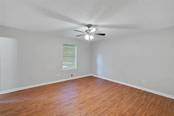 a view of an empty room with wooden floor and a ceiling fan