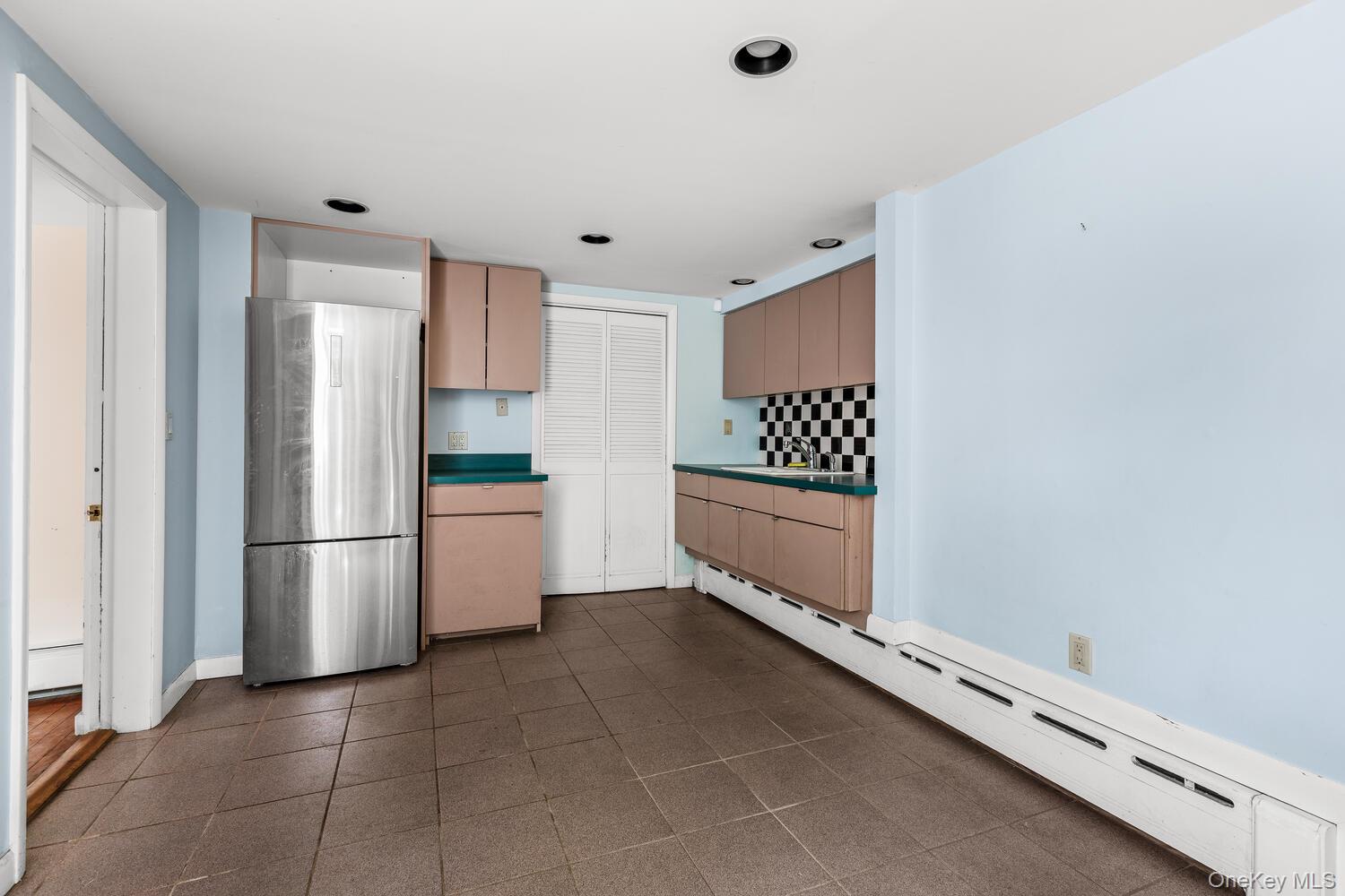 81 Glendale Road Ossining, NY 10562 - Photo 29 of 37 Lower level summer kitchen featuring cast iron baseboard heating, light brown cabinets, freestanding refrigerator, tasteful backsplash, and dark countertops