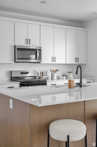 1352 West 2350 South, Unit 18 Perry, UT 84302 - Photo 24 of 26 Modern kitchen featuring white cabinetry, stainless steel microwave, gas range, and a spacious island with a light-colored countertop