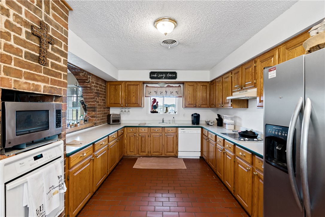 8166 Riley Road Bryan, TX 77808 - Photo 16 of 35 Kitchen with appliances with stainless steel finishes, under cabinet range hood, a textured ceiling, light countertops, and brick floors