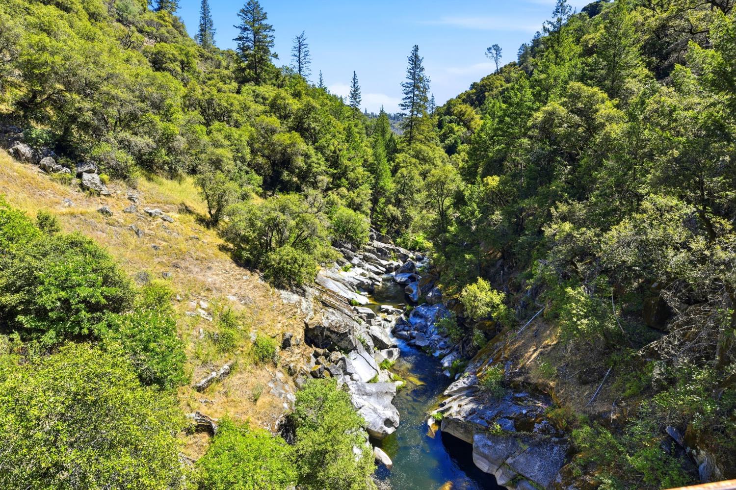 7201 Happy Valley Road Somerset, CA 95684 - Photo 69 of 75 Natural riverine landscape featuring a rocky riverbed with flowing water, bordered by tree-covered slopes. The Middle fork of the Cosumnes River is a magical place to fish, find the best swimming holes and waterfalls.