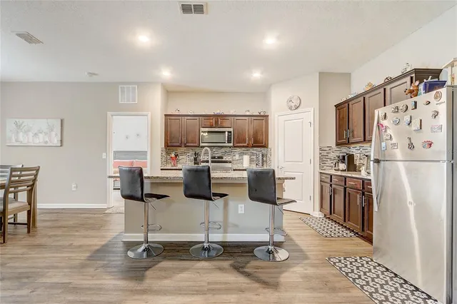 a kitchen with stainless steel appliances granite countertop a stove a sink dishwasher a refrigerator and a dining table with wooden floor