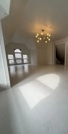 an empty room with wooden floor chandelier and windows