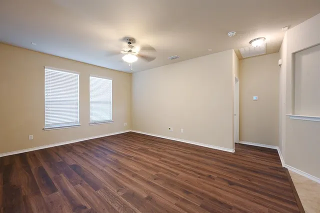 an empty room with wooden floor chandelier fan and windows