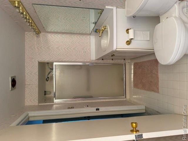 5135 Iron Gate Road Bloomfield Hills, MI 48304 - Photo 16 of 17 Full bathroom featuring a white vanity with integrated sink, gold-tone fixtures, a built-in mirror with overhead lighting, a shower with a frosted glass door, and white square floor tiles