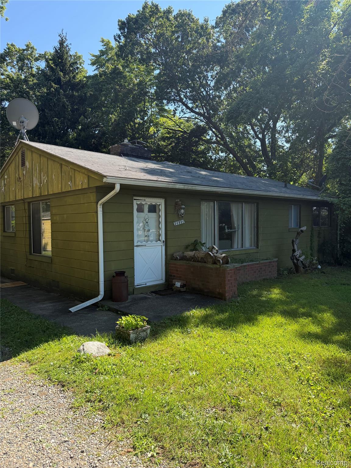 24934 23 Mile Road Macomb, MI 48042 - Photo 2 of 24 Charming cottage with wood-finish siding and a sloped metal roof, featuring a covered front entry, large front-facing windows, and a gravel approach