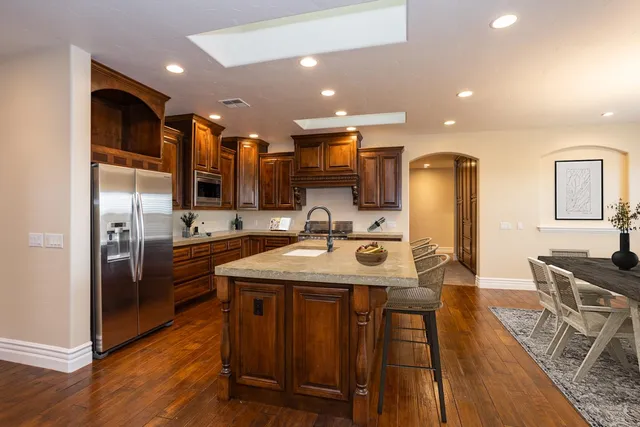 a kitchen with stainless steel appliances granite countertop a sink a stove a refrigerator and island with wooden floor