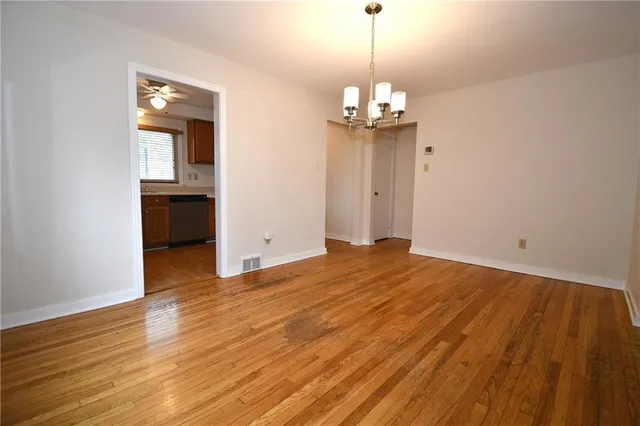 a view of empty room with wooden floor and kitchen view