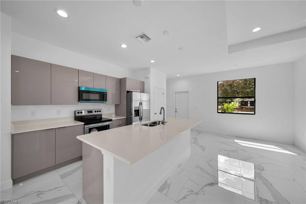 3804 40th Street Southwest Lehigh Acres, FL 33976 - Photo 6 of 24 a kitchen with stainless steel appliances a stove a sink a microwave a refrigerator a white cabinets and a stove