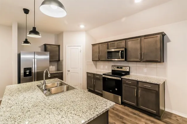 a kitchen with stainless steel appliances kitchen island granite countertop a sink a stove and a refrigerator
