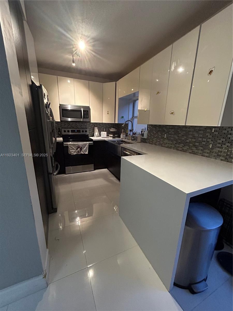 4110 Northeast 24th Street Homestead, FL 33033 - Photo 4 of 16 a kitchen with stainless steel appliances a refrigerator a sink a stove a microwave oven with white cabinets and wooden floor