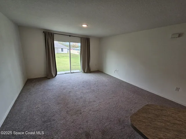 a view of an empty room with a window and a kitchen