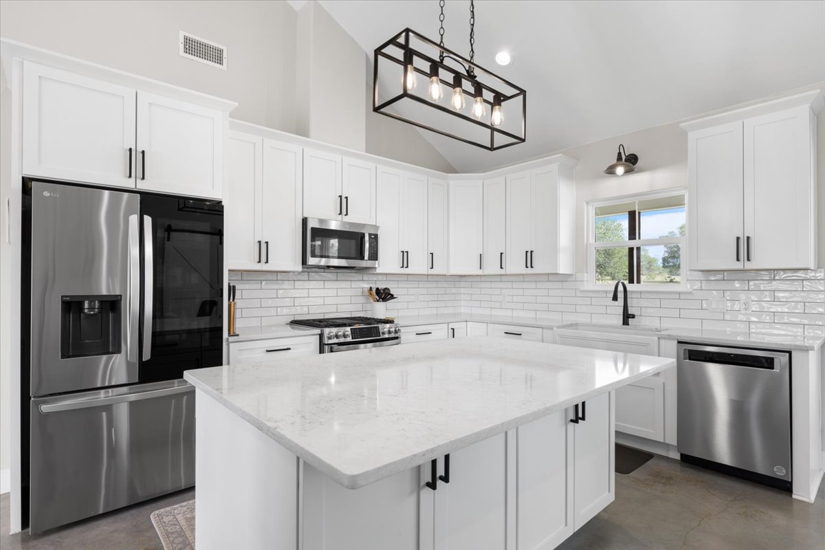 3389 Sparta Field Road Waelder, TX 78959 - Photo 7 of 40 Kitchen featuring stainless steel appliances, finished concrete floors, white cabinets, a kitchen island, and light stone countertops