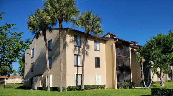 a view of a white house with a big yard and potted plants and trees