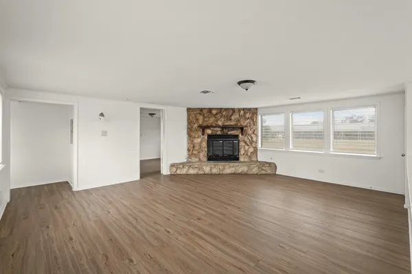 an empty room with wooden floor fireplace and windows