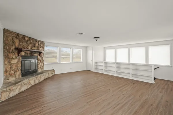 an empty room with wooden floor fireplace and windows
