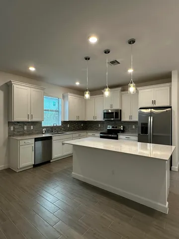 a large white kitchen with a refrigerator a stove top oven a sink dishwasher and white cabinets with wooden floor