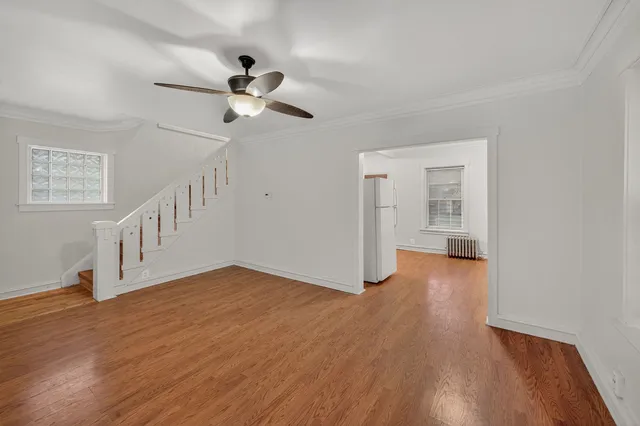 a view of an empty room with wooden floor and a ceiling fan