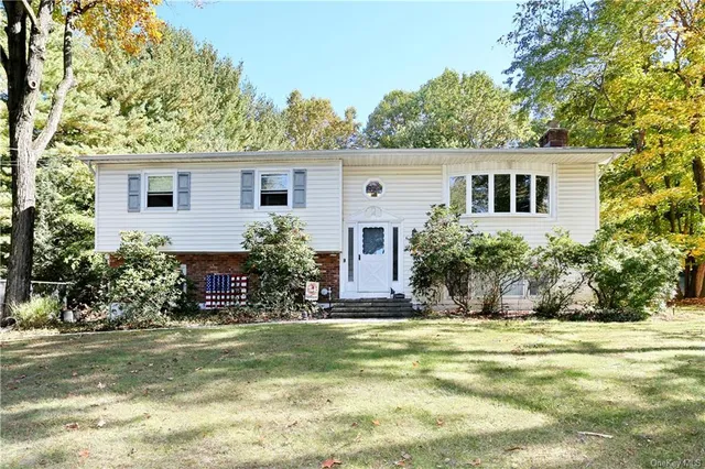 a view of house in front of a yard with potted plants and large trees