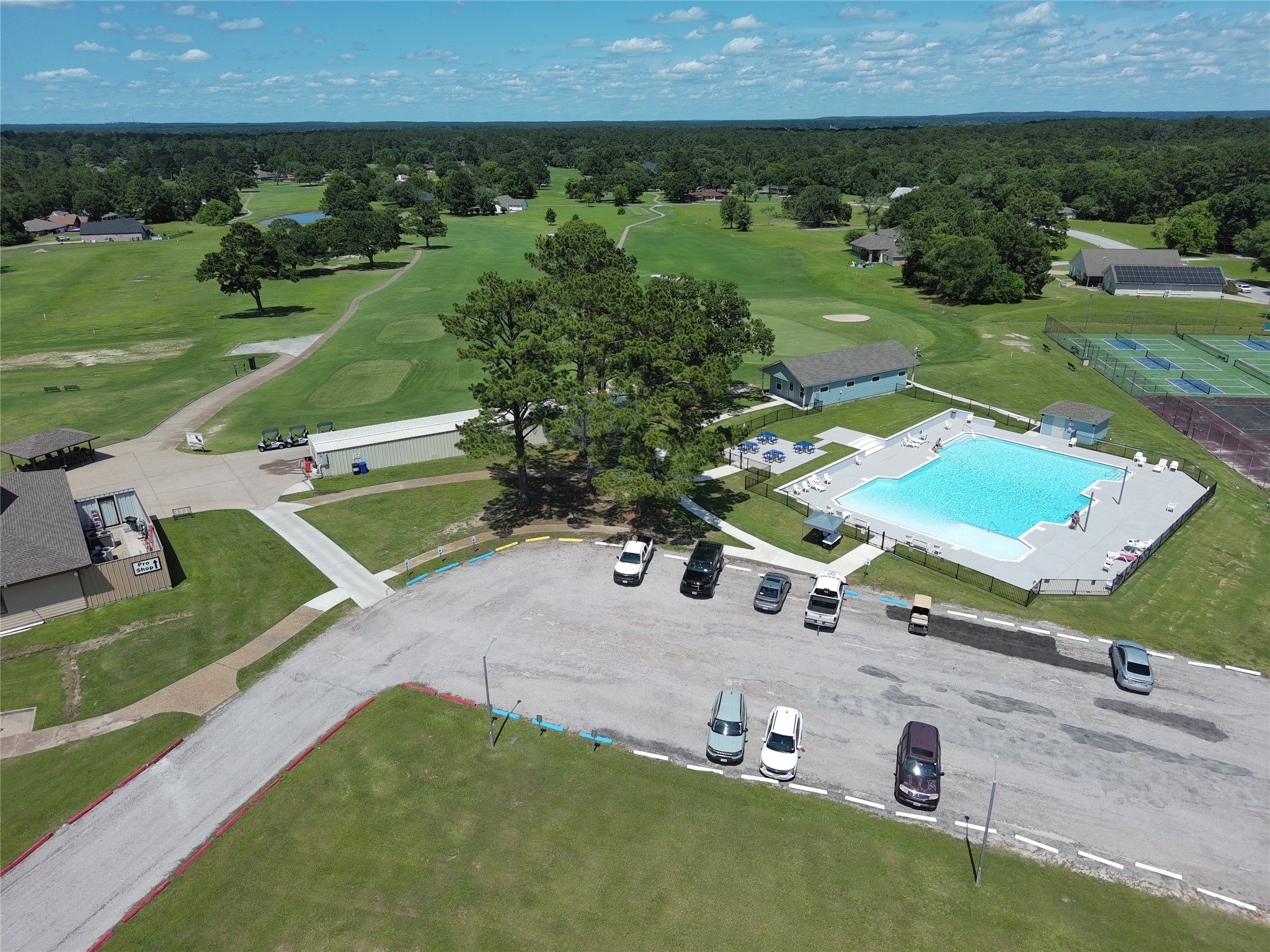 59 Oakridge South Trinity, TX 75862 - Photo 6 of 10 This aerial view showcases a community center with a large swimming pool, tennis courts, and open green spaces, ideal for outdoor activities. The area is surrounded by trees, offering a scenic and tranquil environment, perfect for families and recreation.