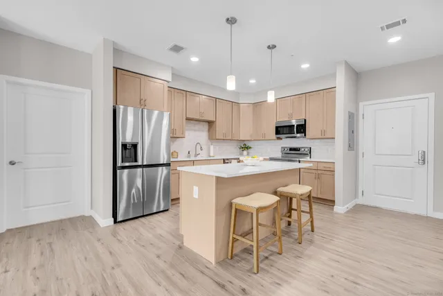 a kitchen with stainless steel appliances granite countertop a refrigerator a sink dishwasher a stove and white cabinets with wooden floor