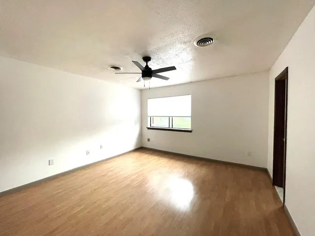an empty room with wooden floor chandelier fan and windows