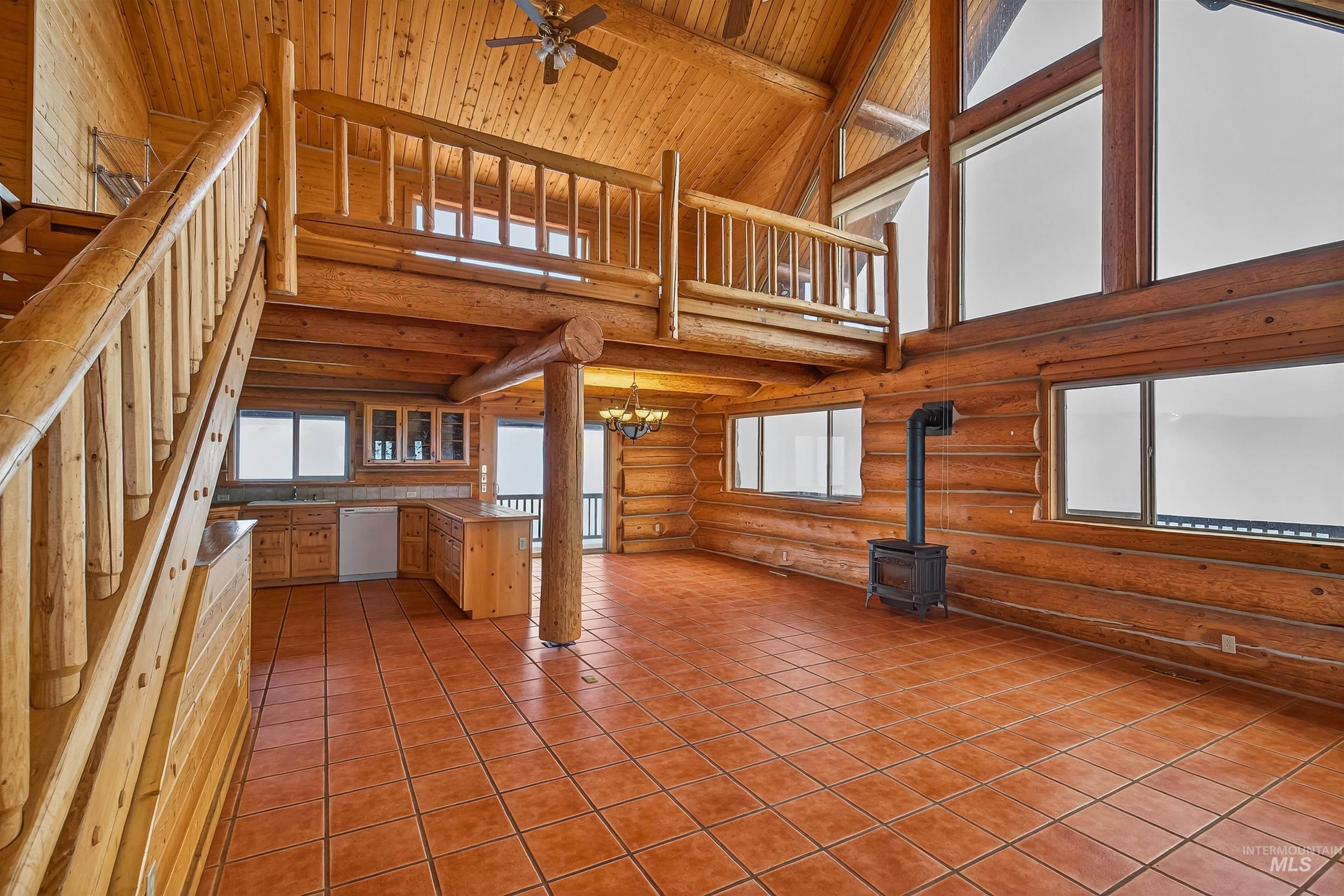 915 Doumecq Road White Bird, ID 83554 - Photo 12 of 49 Unfurnished living room with a high wood beamed ceiling, ceiling fan, a wood stove, suspended lighting, and log walls