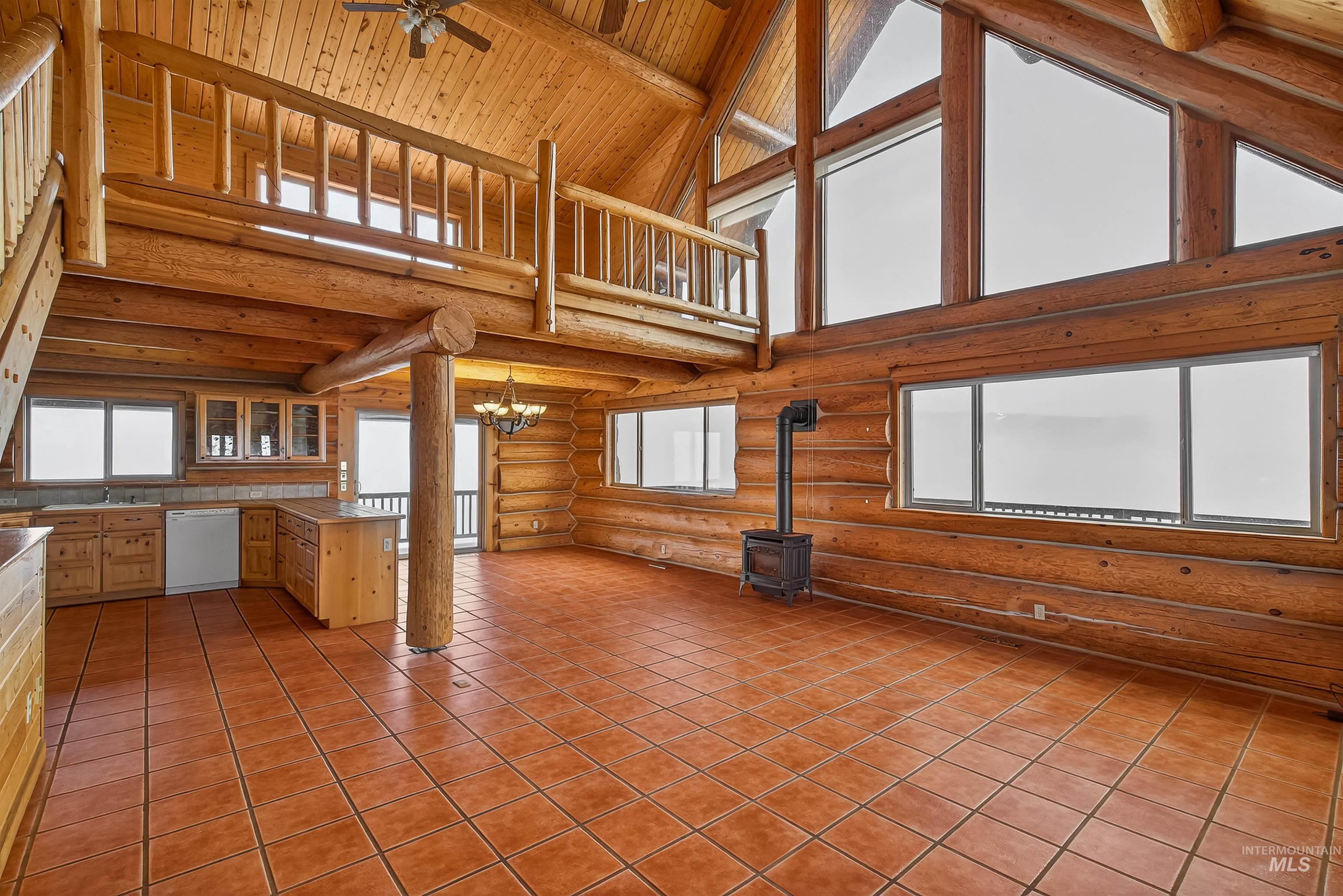 915 Doumecq Road White Bird, ID 83554 - Photo 13 of 49 Unfurnished living room featuring a ceiling fan, suspended lighting, a high wood beamed ceiling, log walls, and a wood stove