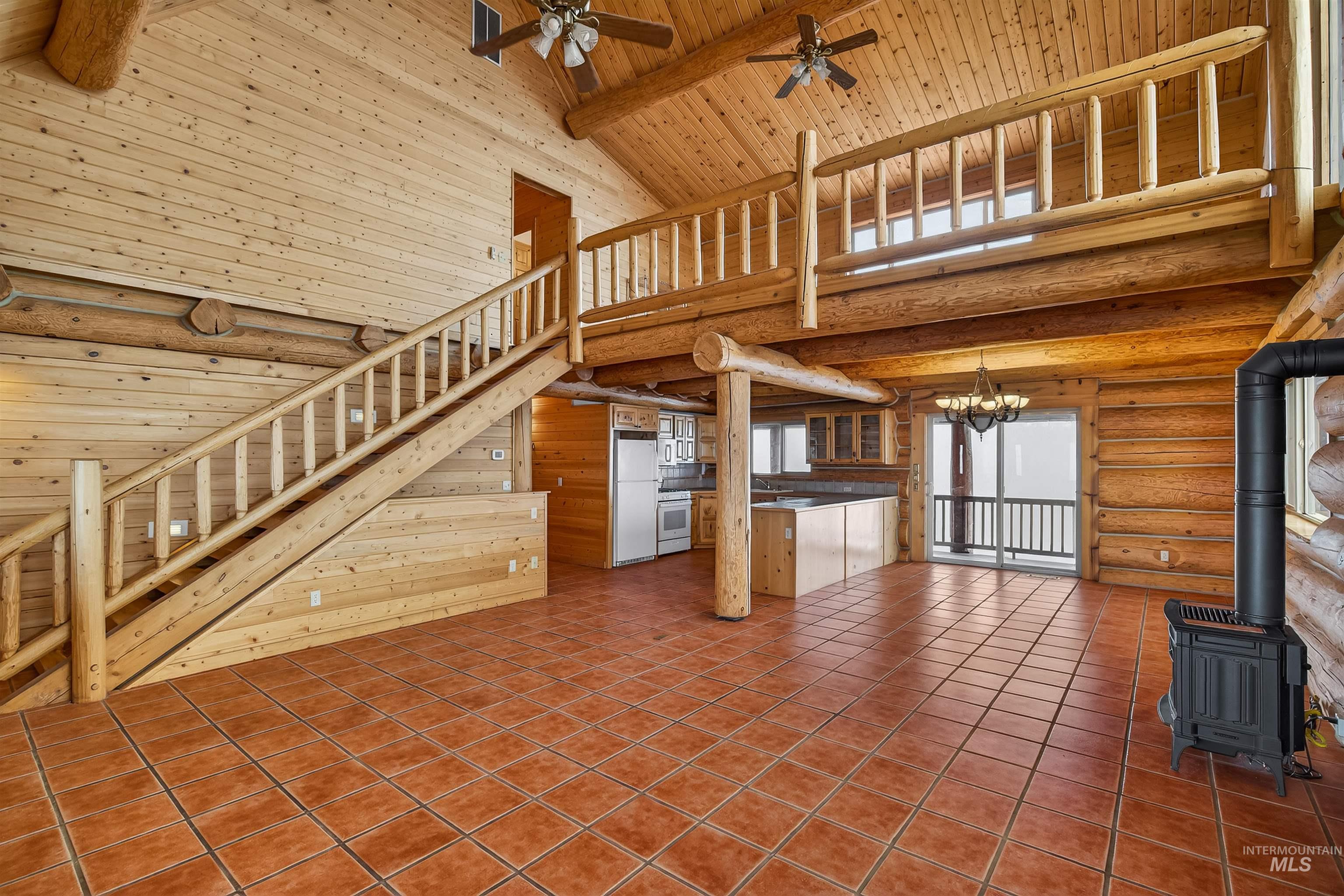 915 Doumecq Road White Bird, ID 83554 - Photo 14 of 49 Unfurnished living room with log walls, a wood stove, a ceiling fan, hanging lights, and a high wood beamed ceiling