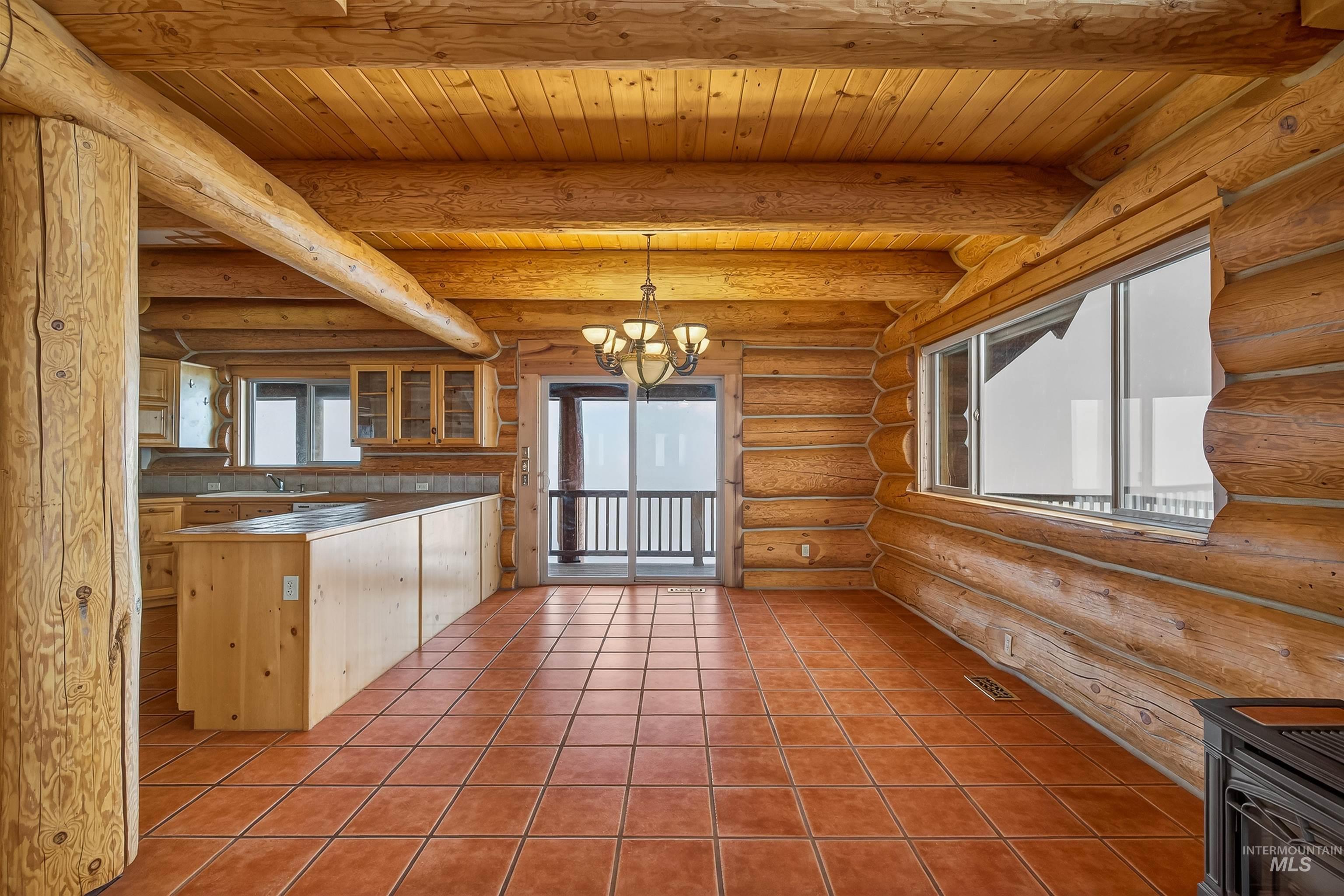 915 Doumecq Road White Bird, ID 83554 - Photo 16 of 49 Kitchen featuring log walls, a chandelier, glass insert cabinets, a peninsula, and a wooden ceiling with exposed beams