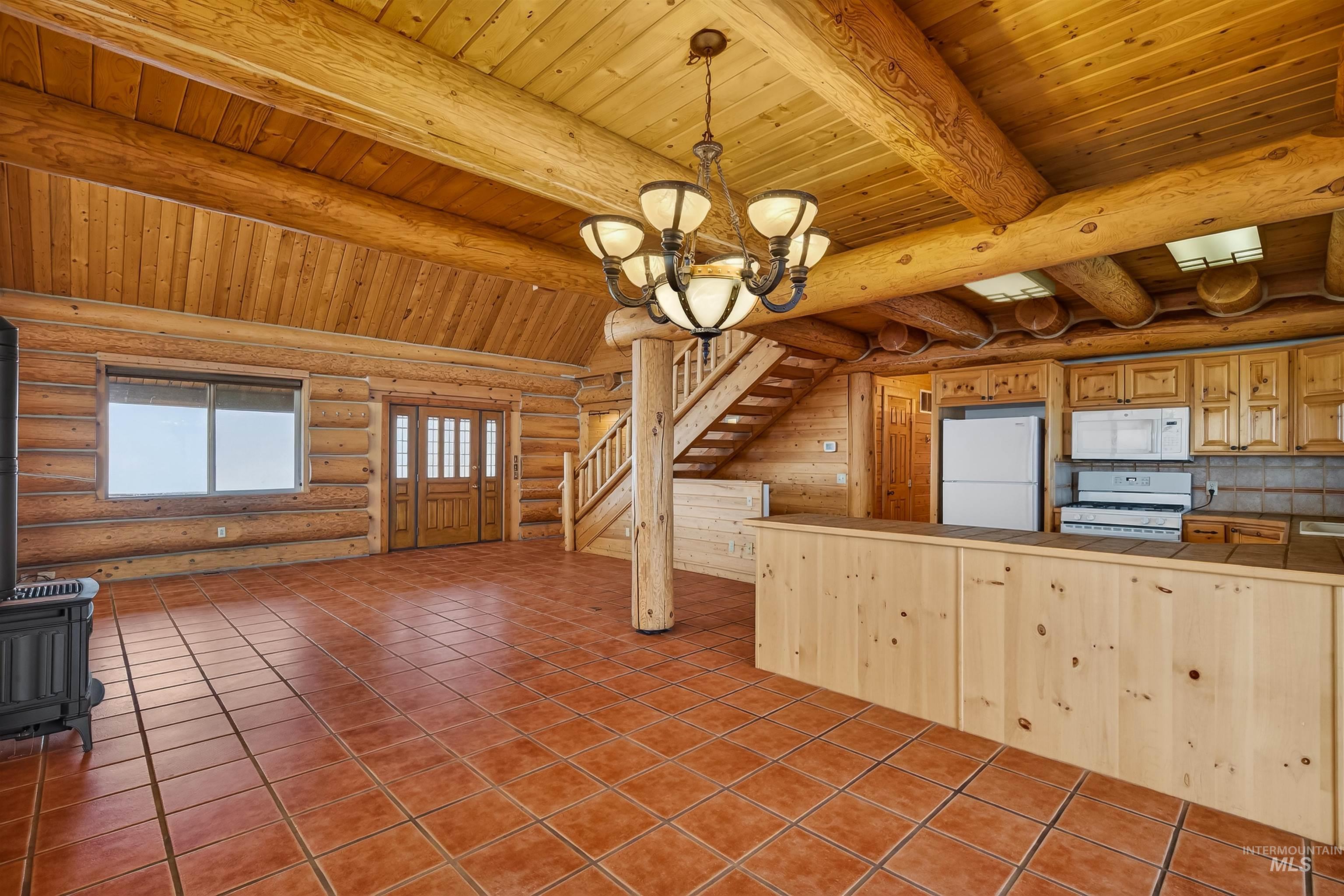 915 Doumecq Road White Bird, ID 83554 - Photo 17 of 49 Kitchen with rustic walls, a wood stove, suspended lighting, white appliances, and a wood ceiling with exposed beams