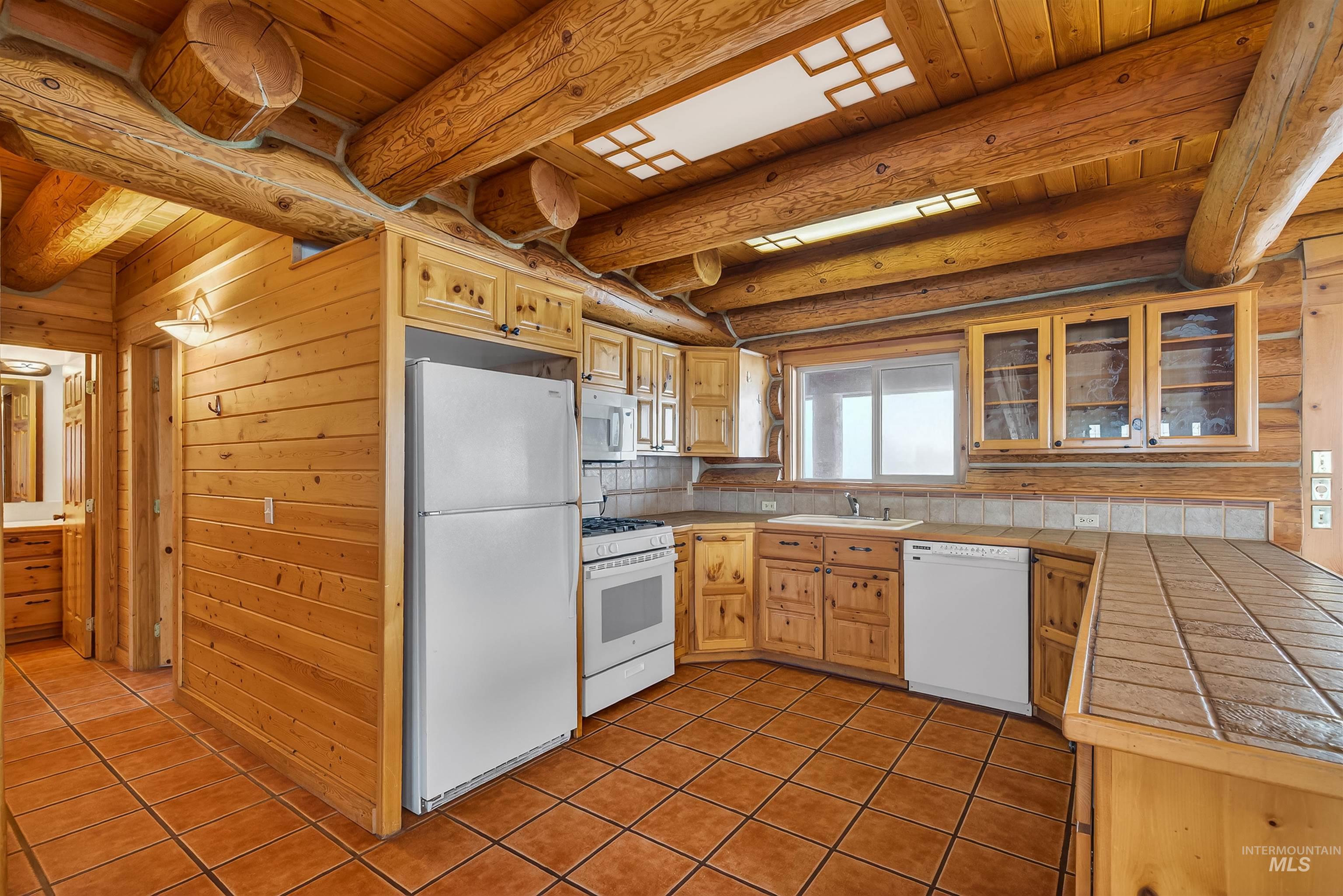 915 Doumecq Road White Bird, ID 83554 - Photo 19 of 49 Kitchen featuring tile counters, white appliances, glass insert cabinets, a wood ceiling with exposed beams, and wood walls