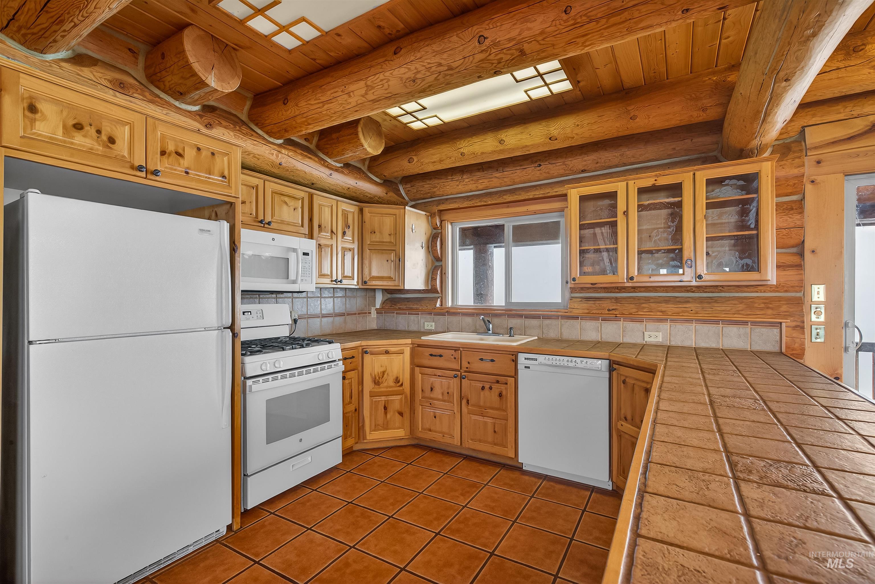 915 Doumecq Road White Bird, ID 83554 - Photo 20 of 49 Kitchen featuring white appliances, glass insert cabinets, tile counters, log walls, and a wood ceiling with exposed beams