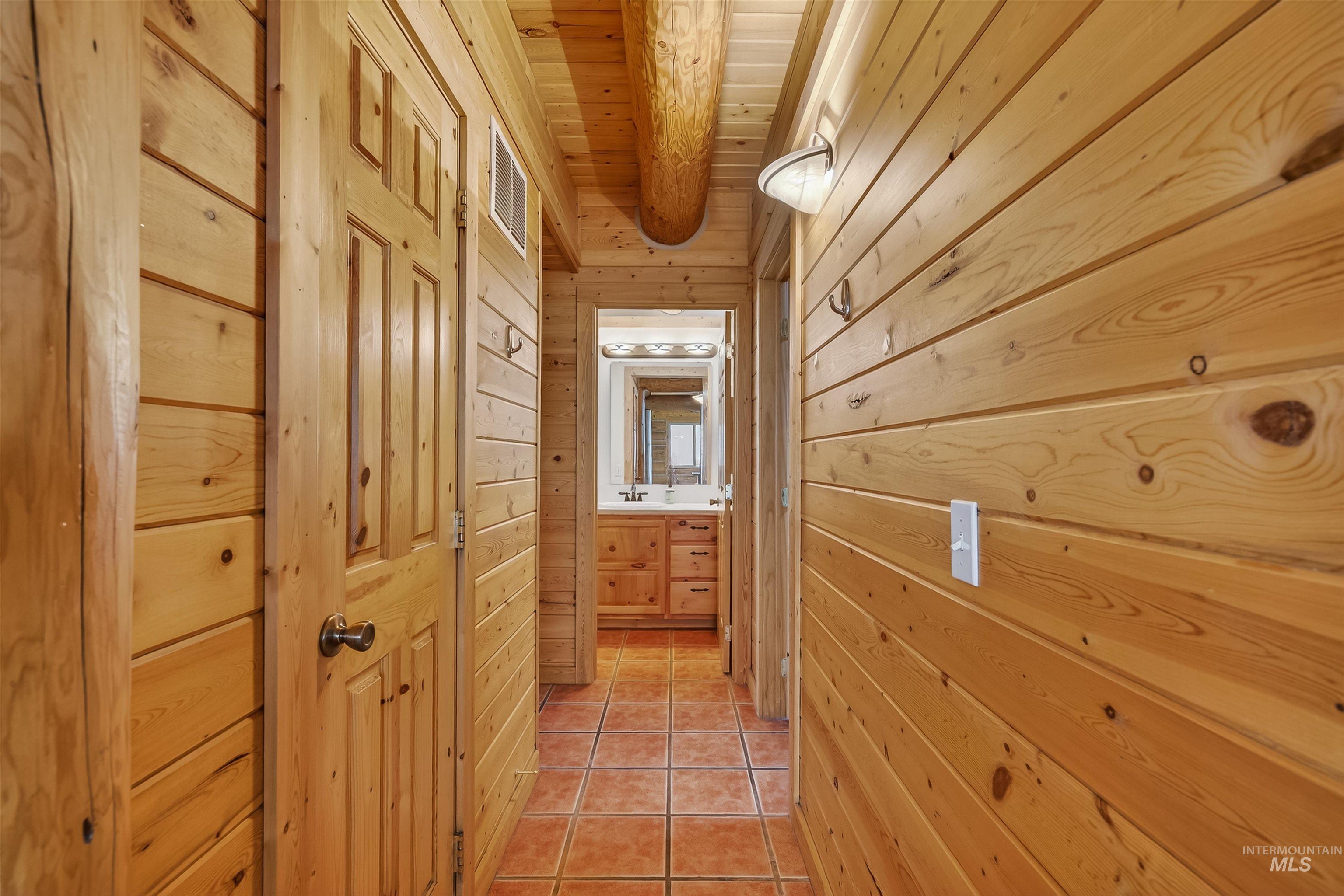 915 Doumecq Road White Bird, ID 83554 - Photo 23 of 49 Hallway featuring light tile patterned flooring, wood walls, and a wood ceiling with exposed beams