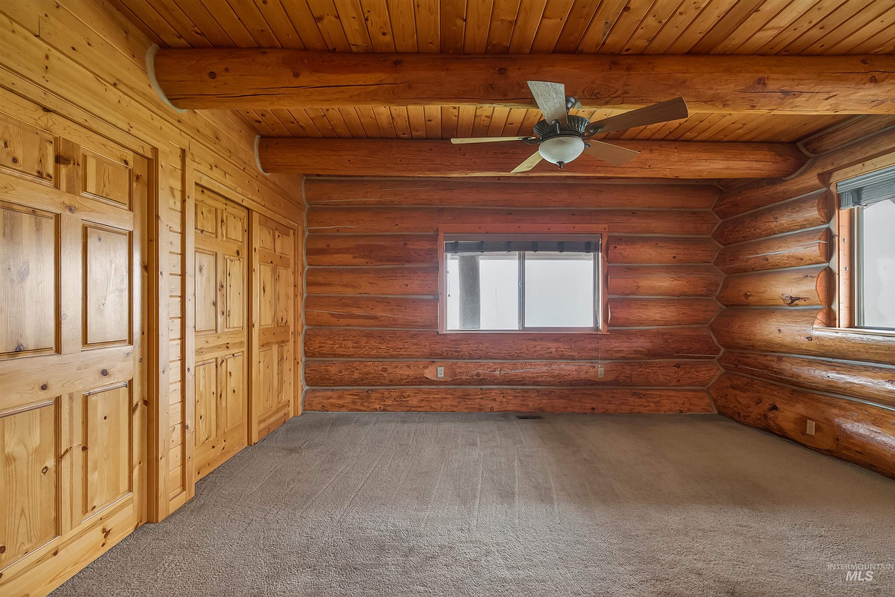 915 Doumecq Road White Bird, ID 83554 - Photo 27 of 49 Unfurnished bedroom with multiple windows, carpet, log walls, a ceiling fan, and a wooden ceiling with exposed beams