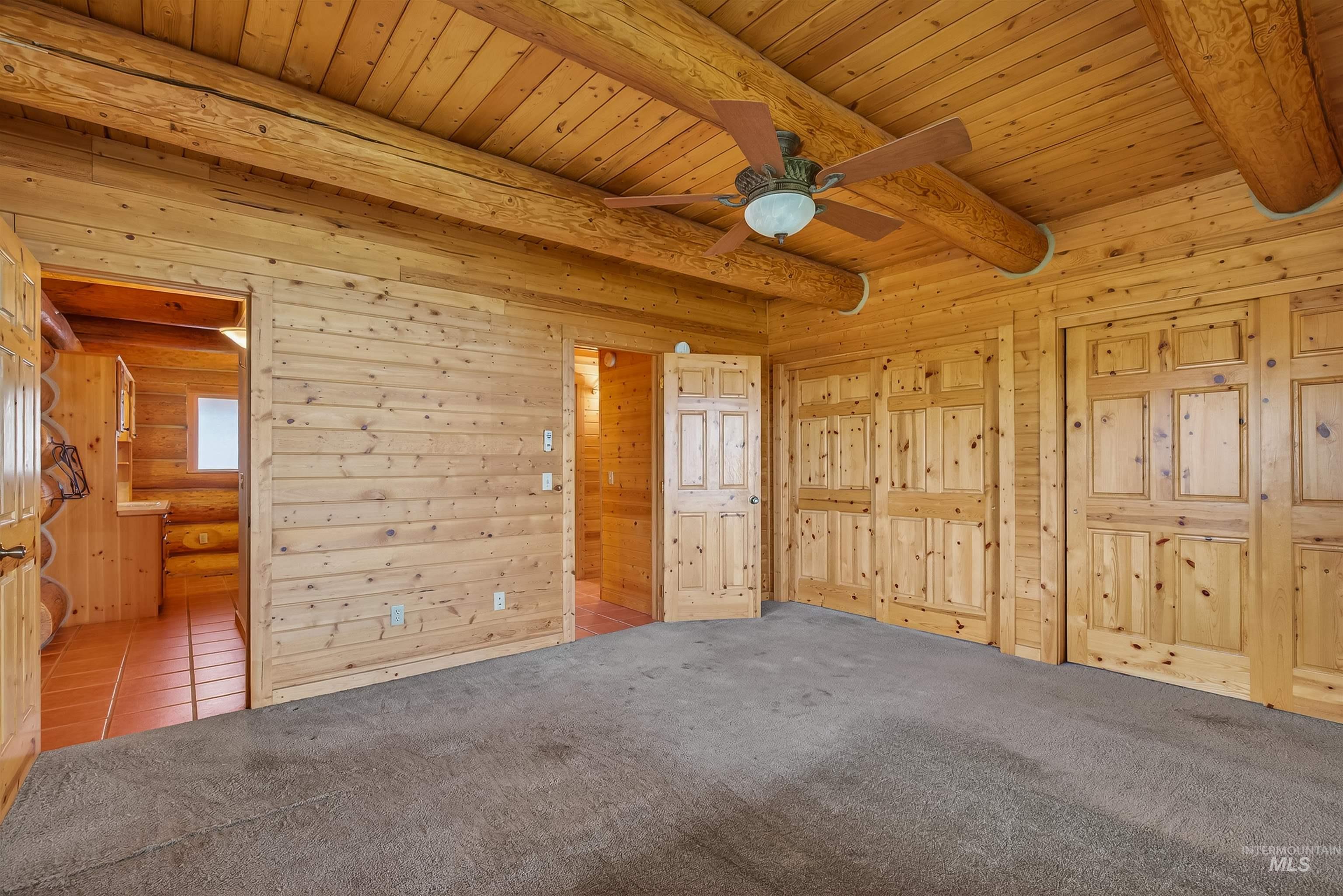 915 Doumecq Road White Bird, ID 83554 - Photo 28 of 49 Unfurnished bedroom featuring carpet, a wooden ceiling with exposed beams, wood walls, ceiling fan, and connected bathroom