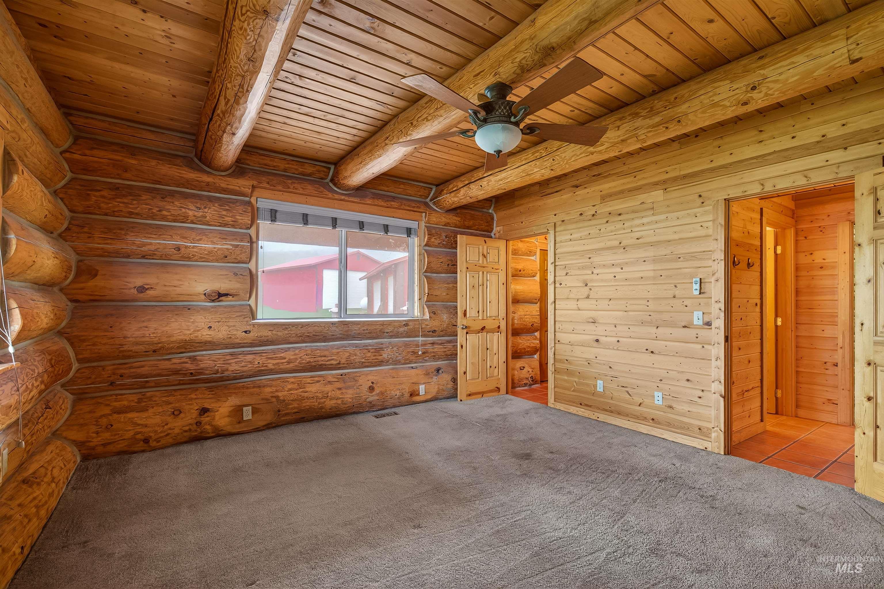 915 Doumecq Road White Bird, ID 83554 - Photo 29 of 49 Carpeted empty room featuring a ceiling fan, log walls, and a wood ceiling with exposed beams