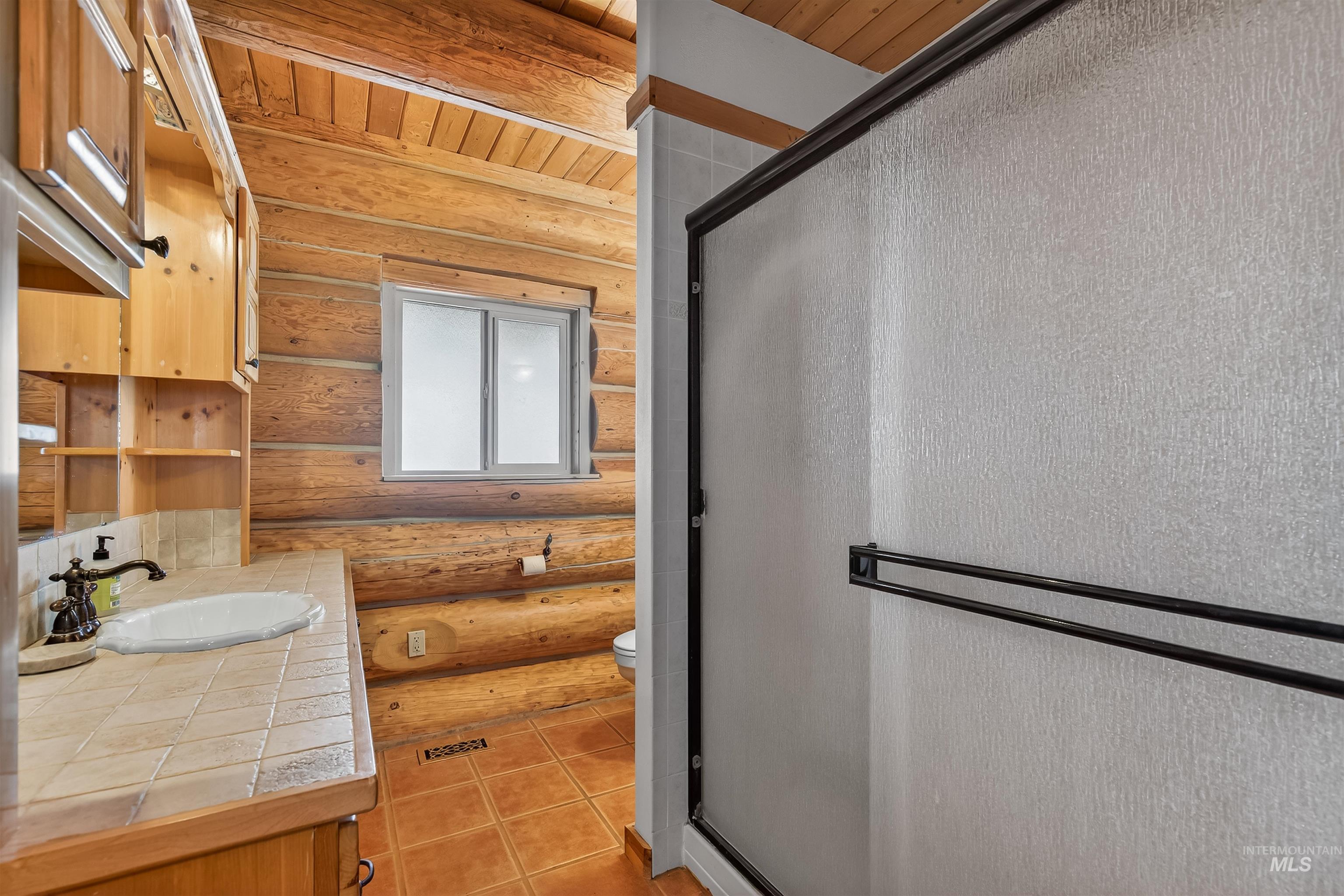 915 Doumecq Road White Bird, ID 83554 - Photo 30 of 49 Full bathroom with vanity, a stall shower, log walls, wooden ceiling, and light tile patterned floors