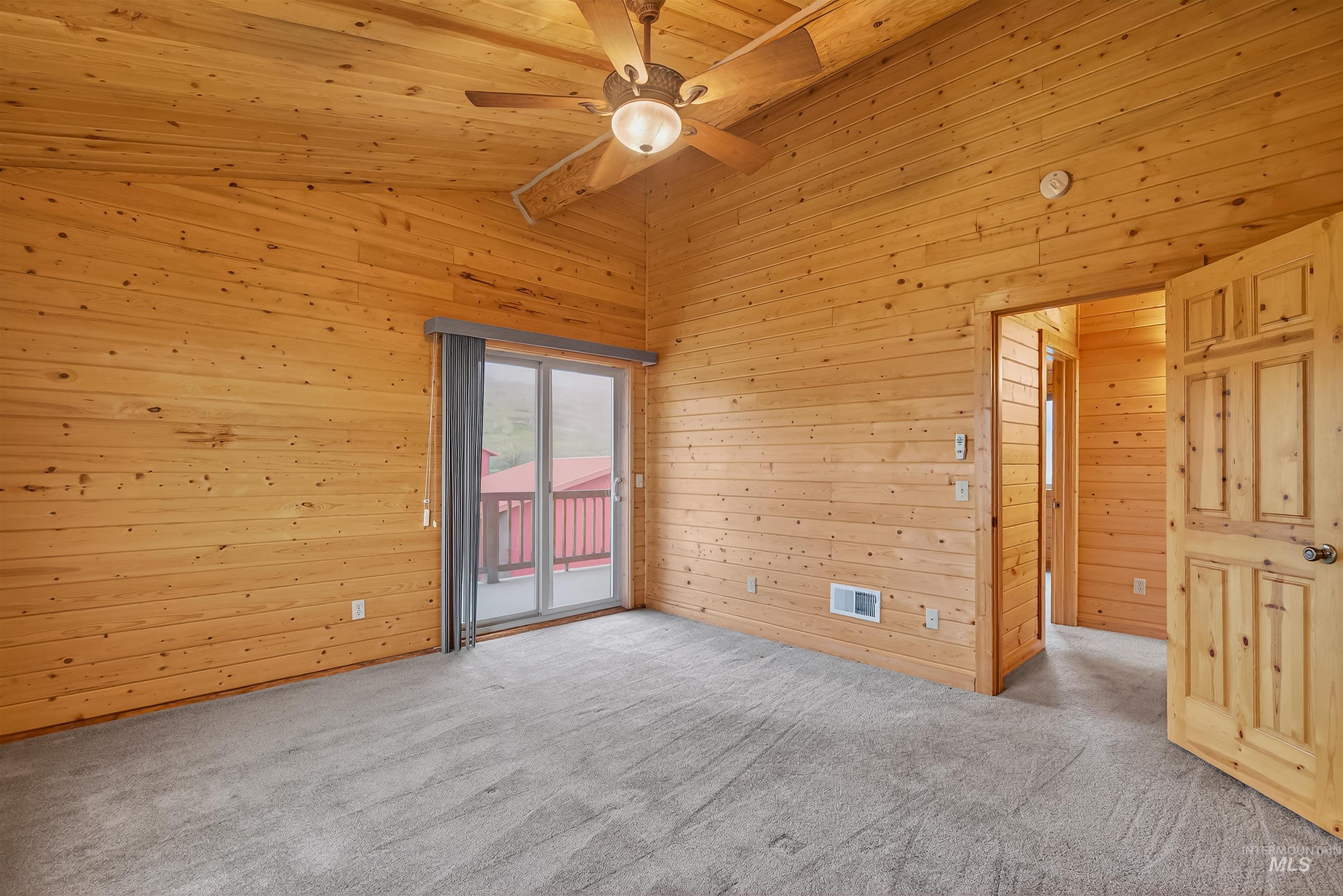 915 Doumecq Road White Bird, ID 83554 - Photo 40 of 49 Empty room featuring light colored carpet, wood walls, a ceiling fan, and a high wood beamed ceiling