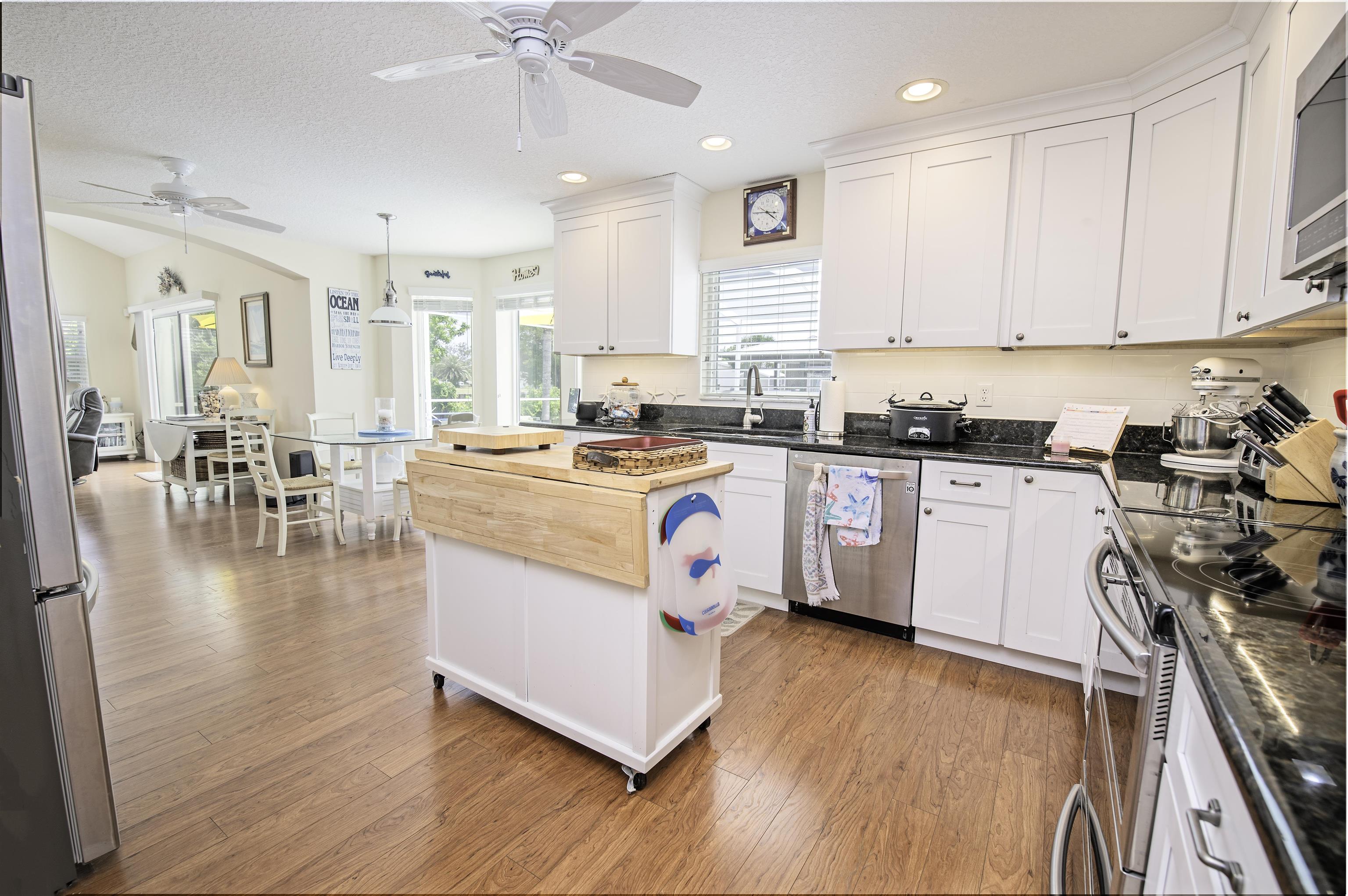253 Treasure Beach Road St. Augustine, FL 32080 - Photo 20 of 52 a kitchen with stainless steel appliances a white stove top oven a sink a dining table and chairs with wooden floor
