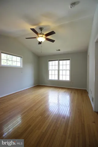 an empty room with wooden floor chandelier fan and windows