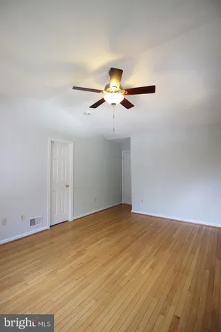 an empty room with wooden floor fan and windows