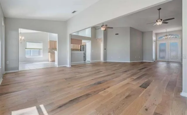 a view of an empty room with wooden floor and a ceiling fan