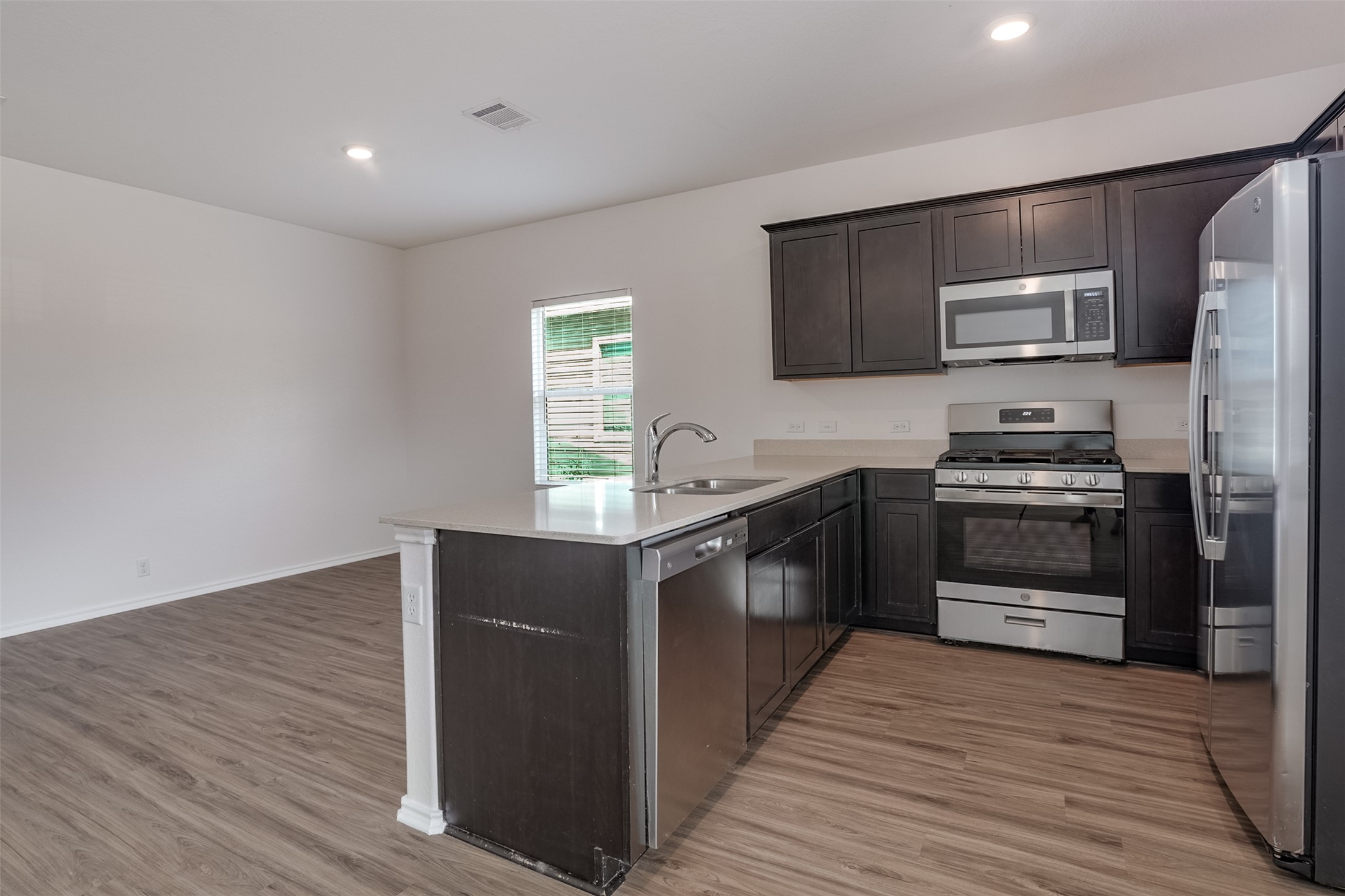 428 Gabbro Gardens Maxwell, TX 78656 - Photo 4 of 26 Kitchen with stainless steel appliances, a peninsula, light wood-type flooring, dark wood finish cabinets, and recessed lighting